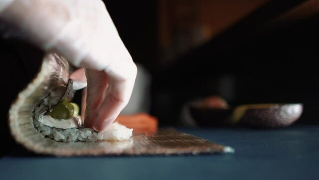 Master sushi maker makes sushi rolls from nori rice and red fish, the process of preparing Japanese food close-up, orange salmon trout fish