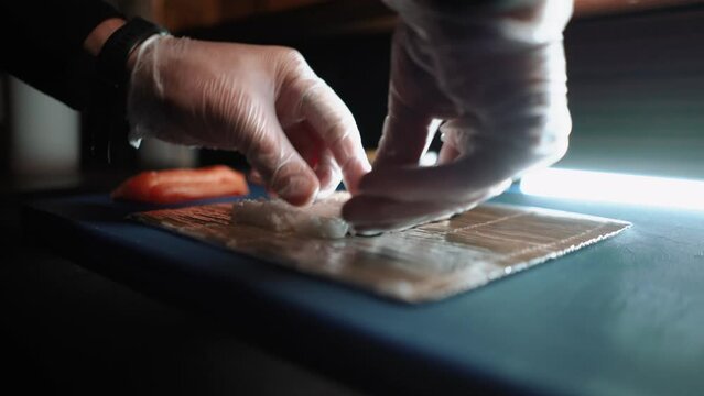 Master sushi maker makes sushi rolls from nori rice and red fish, the process of preparing Japanese food close-up, orange salmon trout fish