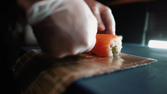 Master sushi maker makes sushi rolls from nori rice and red fish, the process of preparing Japanese food close-up, orange salmon trout fish