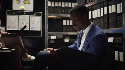Male and female investigators meet in office space to discuss case leads and supporting documentation. Two detectives quest of justice is motivated by expertise, passion, and teamwork. Handheld shot. - obrazy, fototapety, plakaty