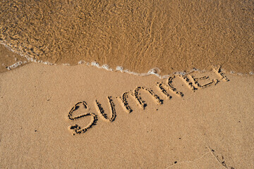 Text SUMMER handwritten in sand surface. Blue ocean wave washing away message at the beach. Summer holidays beach writing vacation concept