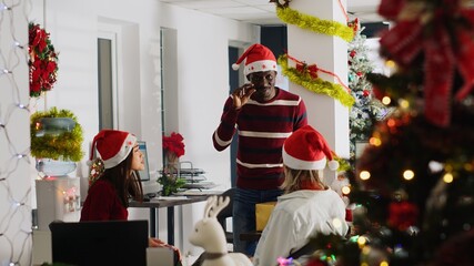 African american employee wearing Christmas hat entertaining coworkers by playing pretending game...