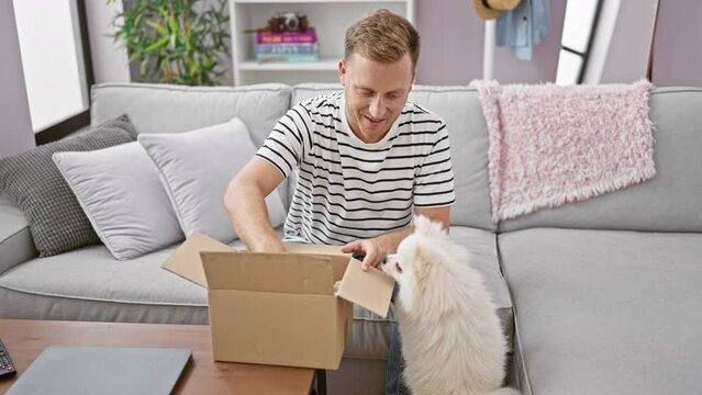 Confident young caucasian man happily unpacking a surprise teddy bear from a cardboard box at home, his adorable dog sitting by, all captured in a cosy indoor setting