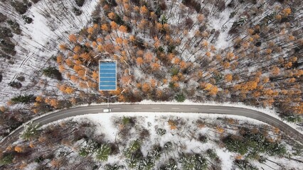 Aerial top down of white electric car driving through winter landscape with graphics showing battery levels