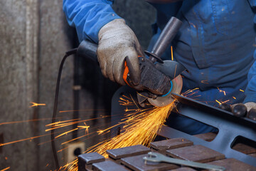 Worker cuts metal with an abrasive disk while grinding iron in industrial factory with spark