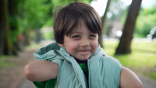 Portrait of a cute little boy standing outside at park smiling at camera and playing with hoodie jacket. Adorable expression