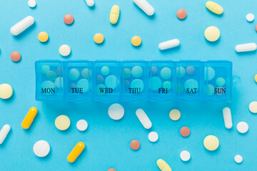 Daily pill organizer with medications on color background, top view
