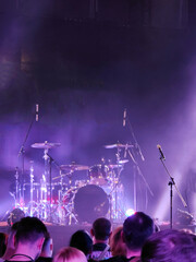 On the stage is a drum set at a concert with a brightly lit stage. The show is visible from the hall