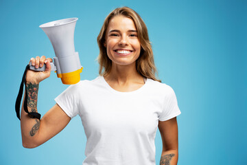 Smiling beautiful woman wearing white t shirt looking at camera holding megaphone standing - obrazy, fototapety, plakaty