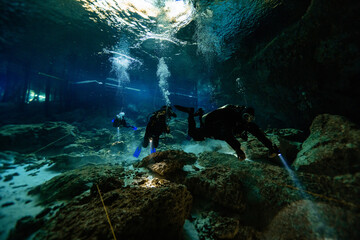 Anonymous Scuba divers with fins, scuba gears and flashlights swimming through the caverns of Cenote Dos Ojos, Mexico
