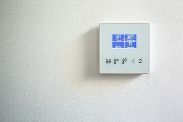 Modern thermostat mounted on white wall at home