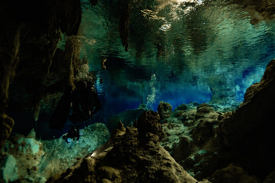Anonymous scuba diver swimming in tranquil waters that mirror the intricate cave ceiling in Cenote Dos Ojos in Mexico
