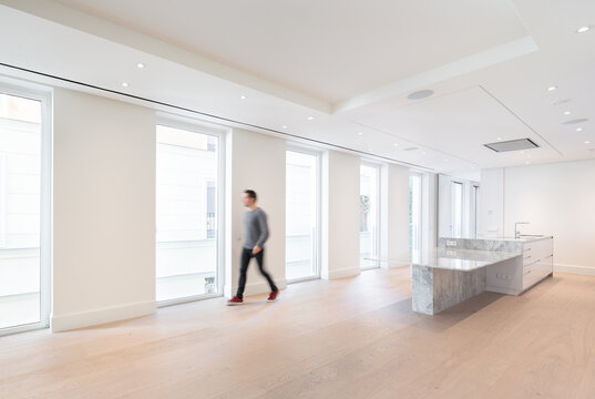 Blurred unrecognizable person walking in a spacious, modern kitchen with marble island and large windows providing ample natural light