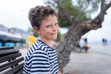 A child in a striped shirt gives a playful glance over his shoulder near a tree-lined promenade