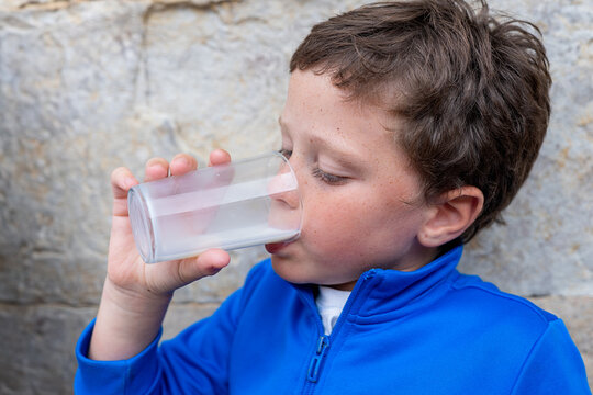 Boy in a blue shirt drinking milk from a glass cup
