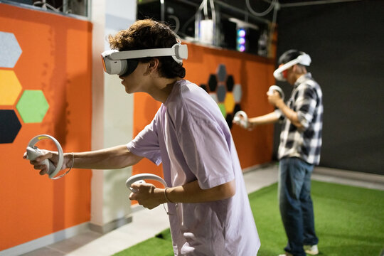 Side view of two friends stand in a gaming area fully immersed in a virtual reality world wearing VR headsets and holding motion controllers