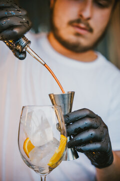 Concentrated young professional barman pouring orange drink in jigger while preparing refreshing cocktail and standing at counter in bar