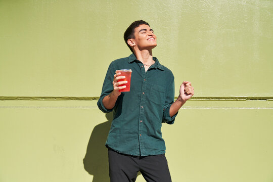 Young man with red iced drink outdoors by green wall