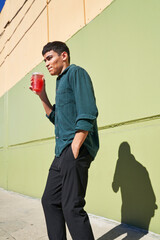 Young man with red iced drink outdoors by green wall