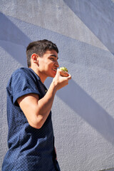 Young man eating avocado toast outdoors by gray textured wall 