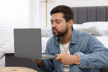 Man sending air kiss during video chat via laptop at home. Long-distance relationship