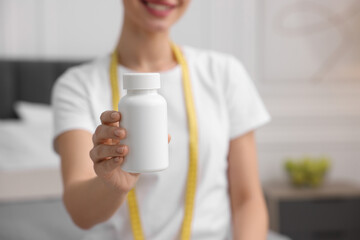 Woman holding bottle of pills in room, closeup. Weight loss