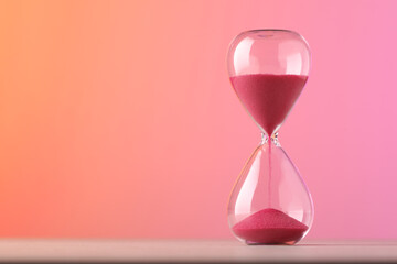 Hourglass with flowing pink sand on table against color background. Space for text