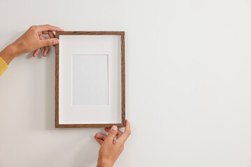 Young man hanging picture frame on white wall indoors, closeup. Space for text