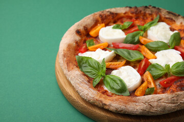 Delicious pizza with burrata cheese, tomatoes and basil on green background, closeup. Space for text