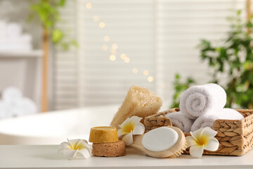 Composition with different spa products and plumeria flowers on white table in bathroom. Space for...