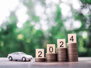 Wooden black with number 2024 on stack of coins and toy car. The concept of saving money for car in new year 2024