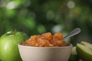 Bowl with delicious apple jam and fresh fruits against blurred background, closeup. Space for text