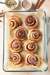 Tasty cinnamon rolls, sticks and nuts on beige textured table, flat lay