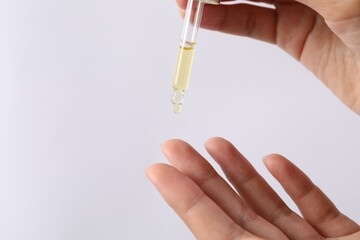 Woman applying cosmetic serum onto her finger on white background, closeup. Space for text