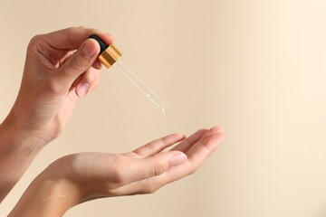 Woman applying cosmetic serum onto her finger on beige background, closeup. Space for text