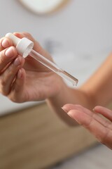 Woman applying cosmetic serum onto her finger on blurred background, closeup
