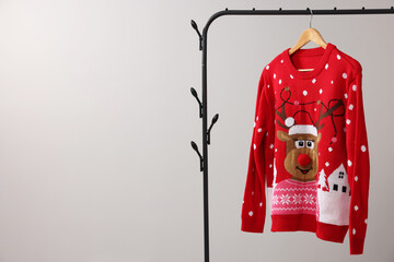 Rack with Christmas sweater on light background, space for text