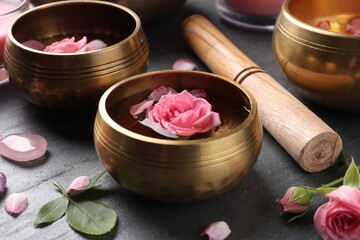 Tibetan singing bowls with water, beautiful rose flowers and mallet on gray table, closeup