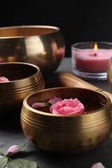 Tibetan singing bowls with beautiful rose flowers, and burning candle on table, closeup