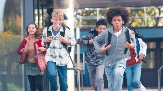 Group of secondary or high school pupils running towards camera outside school building - shot in slow motion