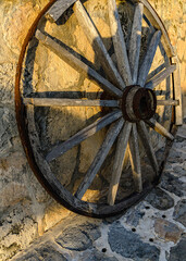 Antique Wooden Wagon Wheel against Stone Wall in Golden Light