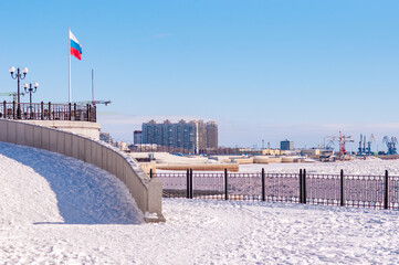 A large Russian flag on the snow-covered embankment of the Amur River on a sunny winter day....