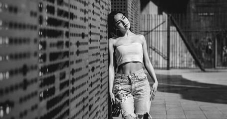 Urban vibes: stylish latino girl in jeans and little top posing against copper wall under sunlight, with big copy space (in black and white)
