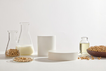 Laboratory glassware filled with soybean milk, oil and soybean seeds arranged with white podiums. Front view. Soybeans (Glycine max) are a superior plant protein choice