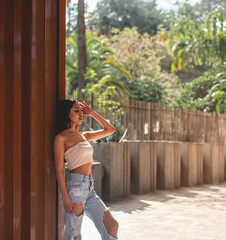 Urban vibes: stylish latino girl in jeans and little top posing against copper wall under sunlight, with big copy space
