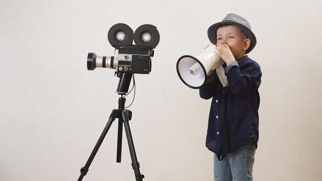 Little boy with megaphone near vintage video camera playing the film director