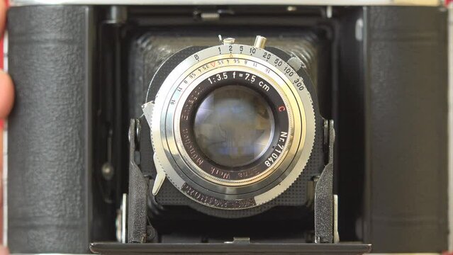 Hand adjusts retro photo camera lens preparing for shooting, front view close detail