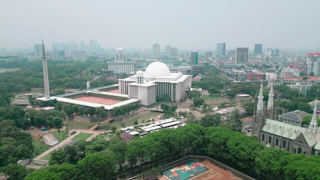 Cinematic aerial view of the iconic Istiqlal Mosque near the Jakarta National Monument or Monas and the Cathedral Church.