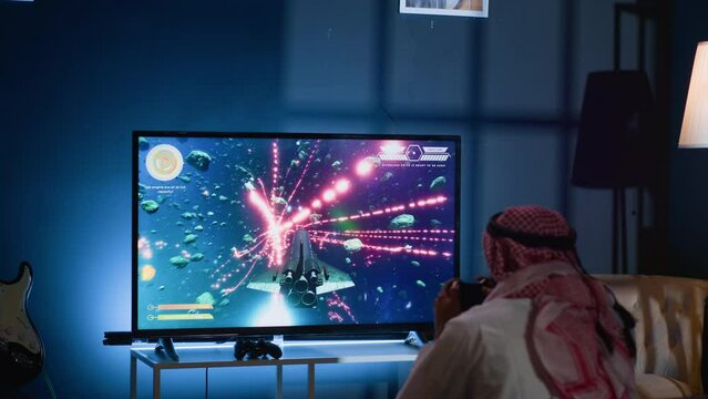 Gamer upset at seeing game over message on TV screen playing arcade space shooter videogame. Man spending time at home on gaming system, frustrated after losing esports competition