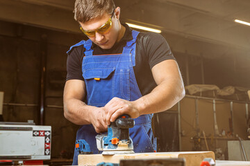 Close up of an young man builder carpenter equals polishes wooden board with a polishing machine or...